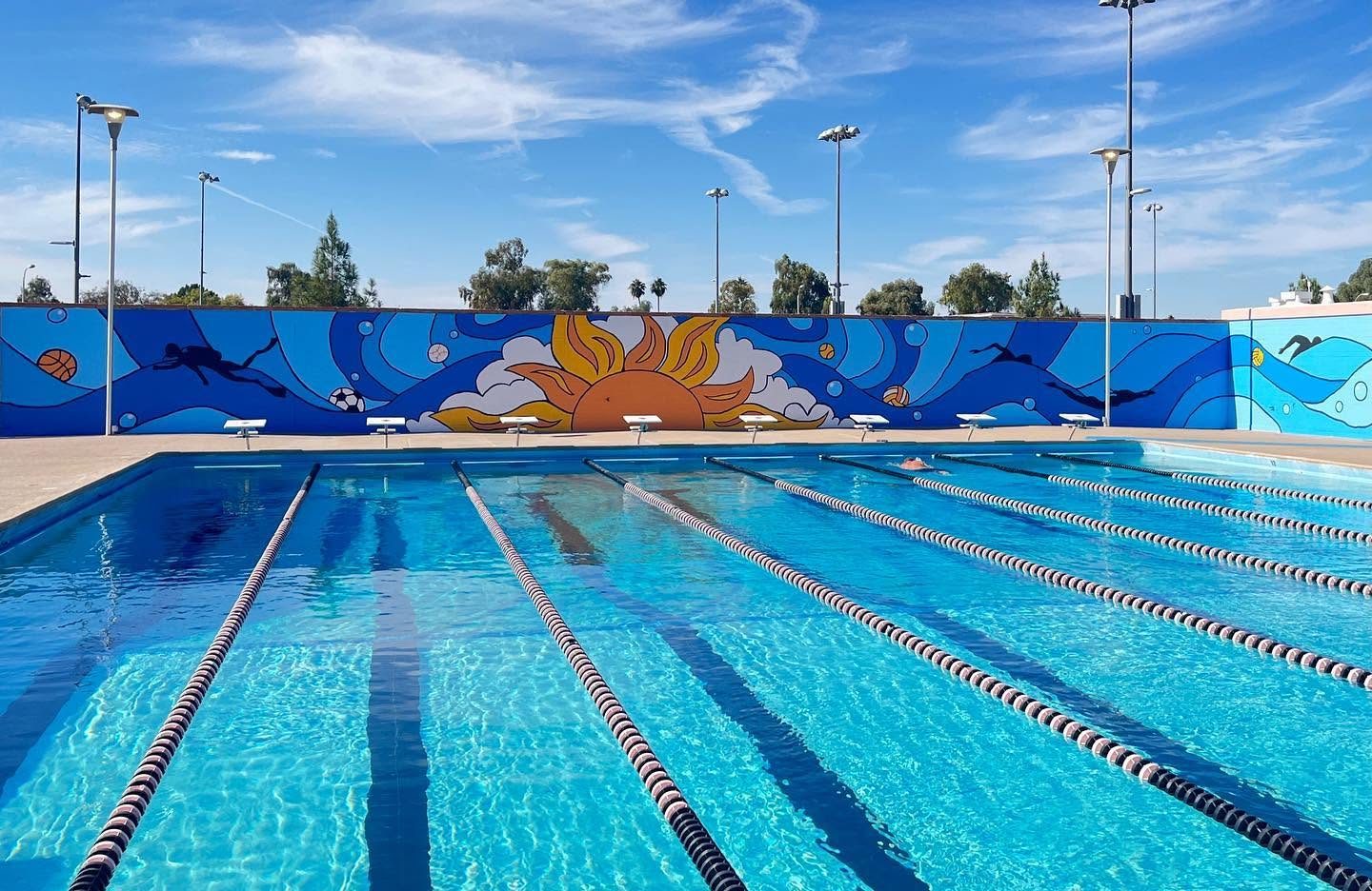 The finished 90-foot mural along the wall at the college pool, showing swimmers, a scuba diver, and a sun in deep blues and orange